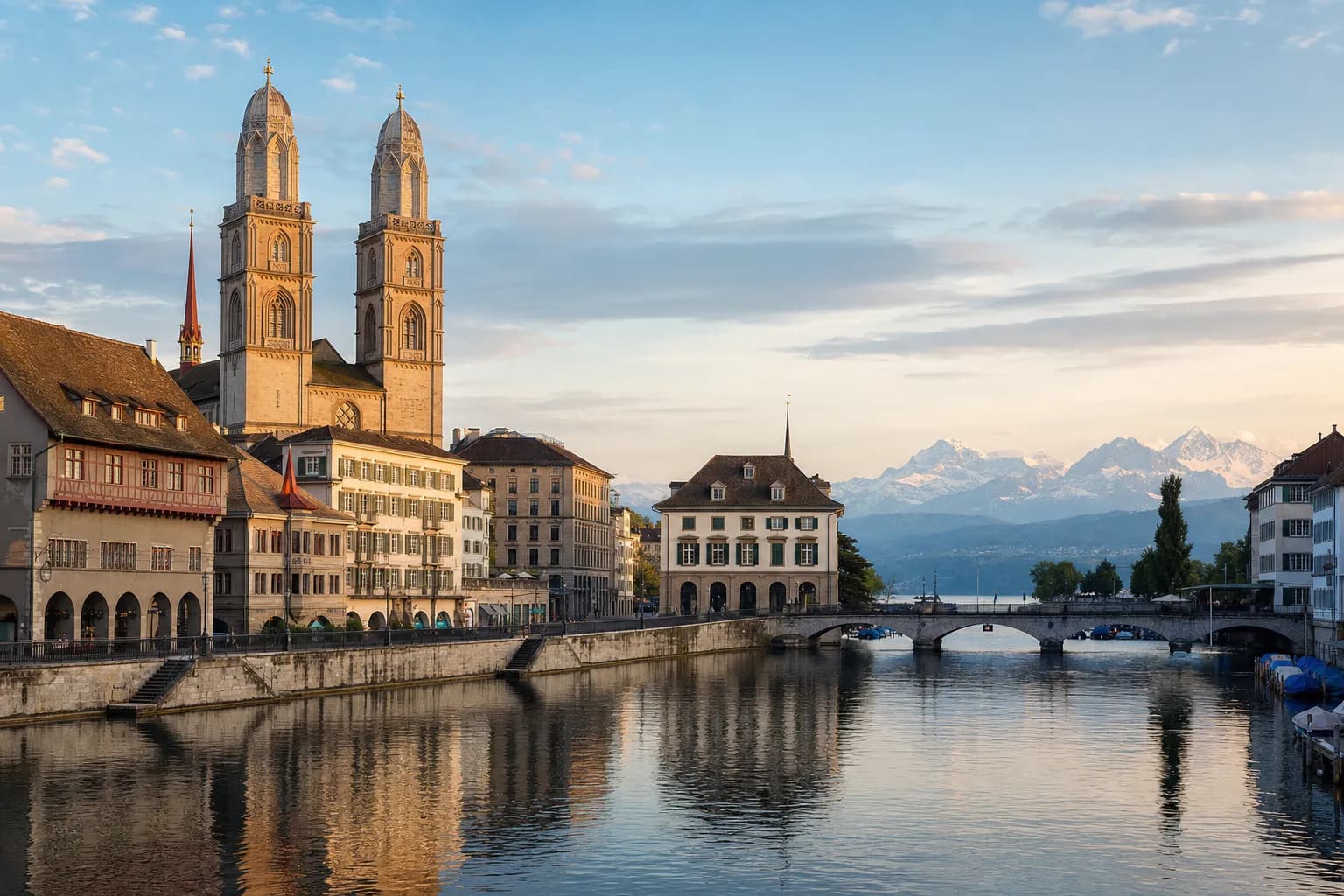 Die Limmat in Zürich mit den Türmen des Grossmünsters, den Quaifassaden und den Alpen in der Ferne